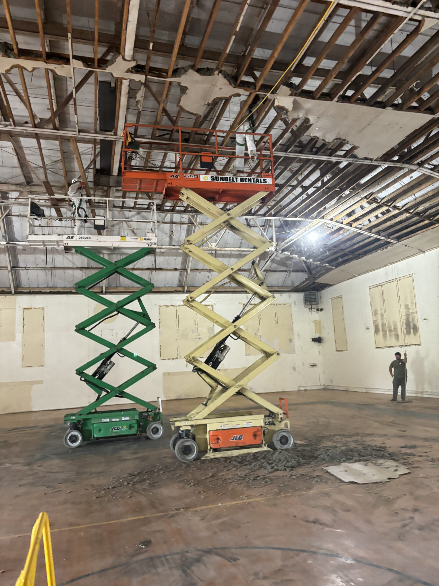 Two scissor lifts in a room with some people standing around.