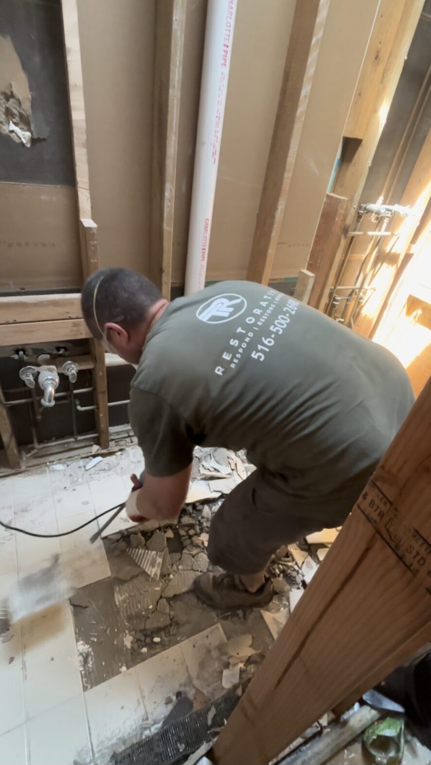 A man in green shirt using a drill on floor.