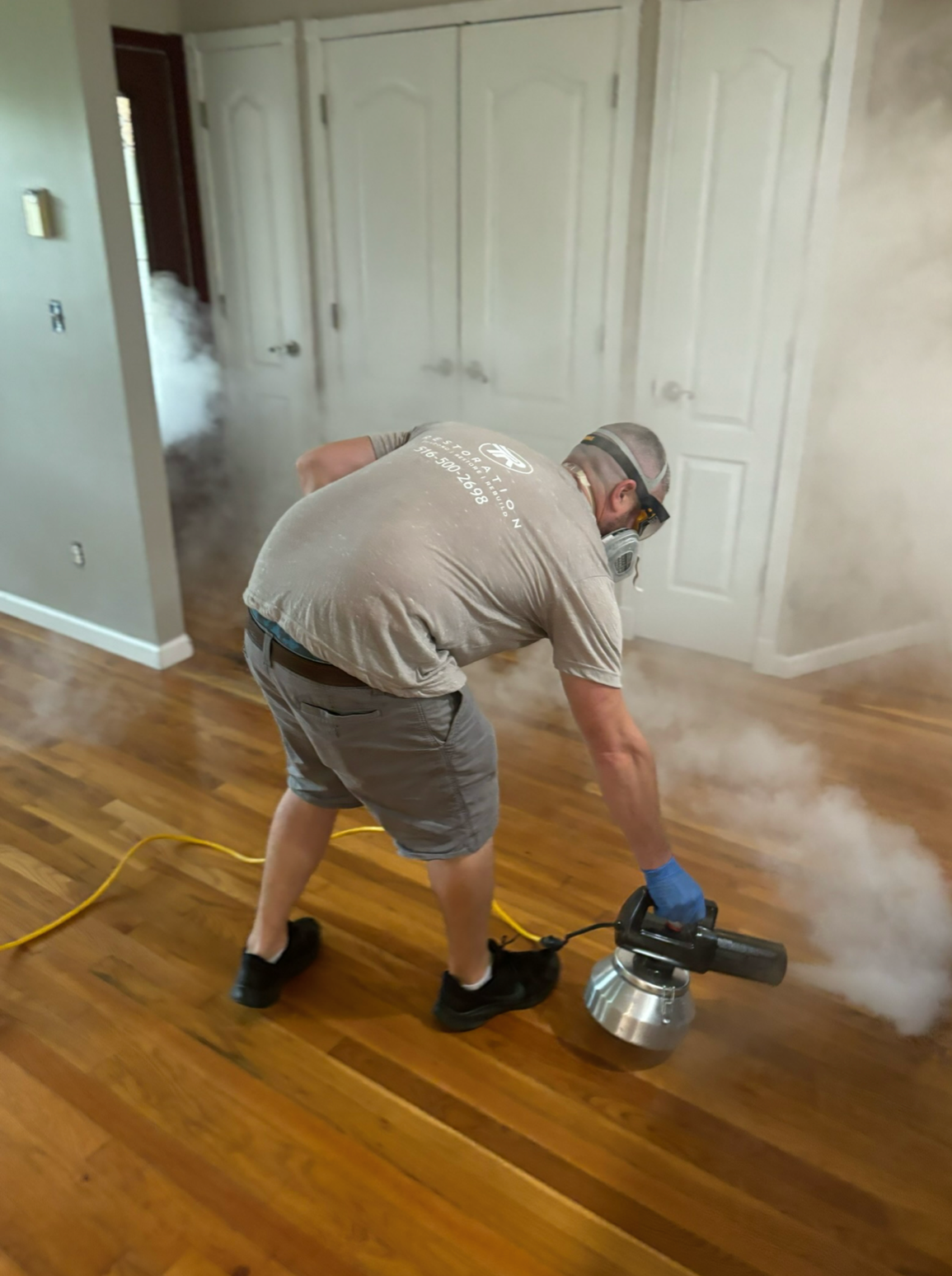 A man in grey shirt and blue shorts using a power tool.