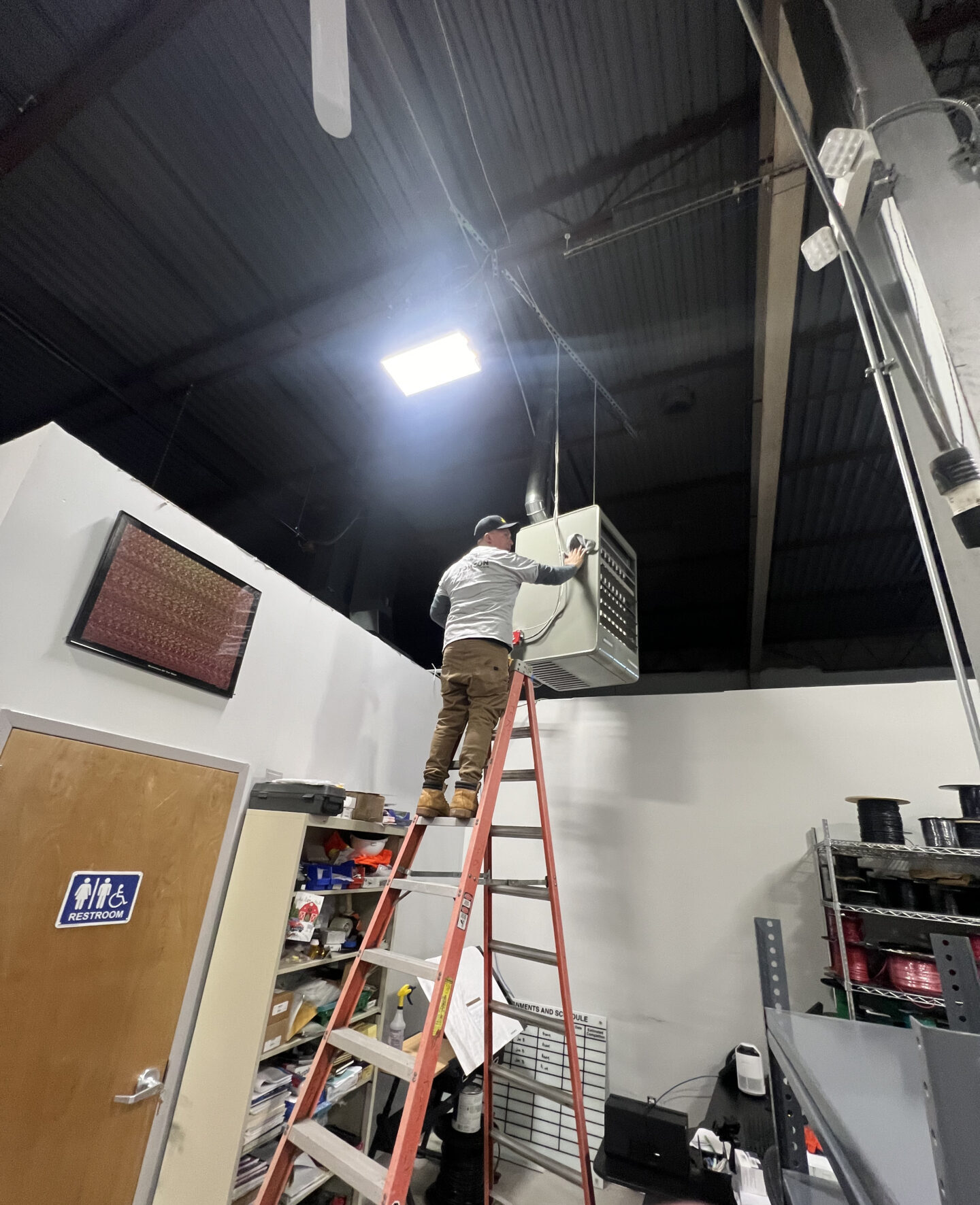 A man on a ladder working on an air conditioner.